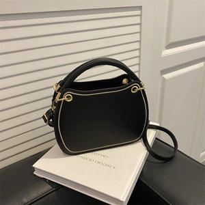 Elegant black top-handle bag with gold trim and shoulder strap on a white book