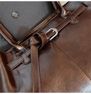 Macro detail of dark brown oil-wax leather tote with silver buckle and fine stitching