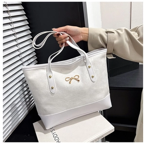 Detail of white canvas tote bag with leather base and elegant gold bow hardware