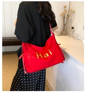 Detail of red oversized tote bag with gold logo lettering and adjustable drawstring sides
