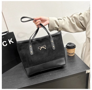Detail of black tote bag featuring a gold bow ornament and suede leather patchwork