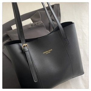 Detailed view of black leather tote bag featuring gold buckle and adjustable strap