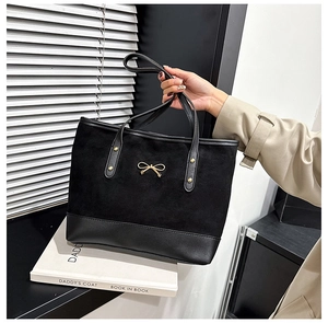 Detail of black tote bag featuring matte leather stitching and gold bow decoration