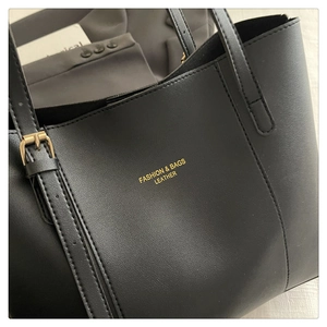 Detail of black leather tote bag featuring gold FASHION & BAGS lettering and metal buckle