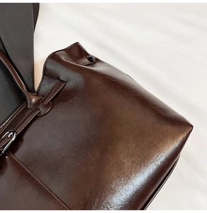 Detail of dark brown tote bag with vintage oil wax leather texture and metal buckle accents