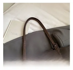 Detail view of deep brown suede tote bag featuring long knotted shoulder straps on bed