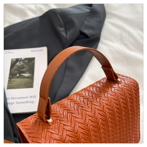 Close-up of brown woven leather bag with gold buckle and smooth handle detail