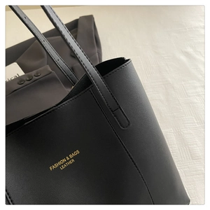 Detailed close-up of black leather tote bag with lychee texture and gold-stamped logo