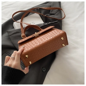 Détail d'un sac à main marron à motif crocodile avec fermoir doré et picots de protection