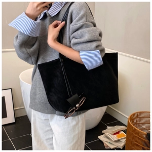 Detail of a large black suede tote bag being worn over the shoulder in a cozy setting