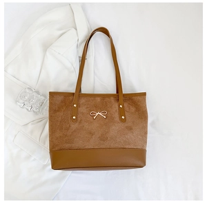 Detail of caramel tote bag featuring suede texture, gold bow and metallic studs
