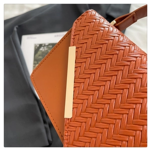 Detail der orangebraunen Webstruktur-Handtasche mit eleganter goldener Metallschnalle