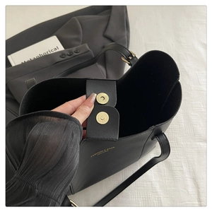 Detail of magnetic snap closure and golden embossed text on black leather tote bag