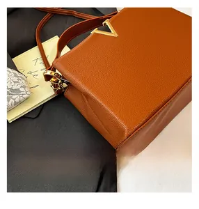 Détail du cuir grainé marron et boucle métallique dorée en V sur le sac à main