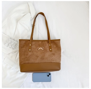 Macro detail of brown suede tote bag with golden bow ornament and reinforced stitching