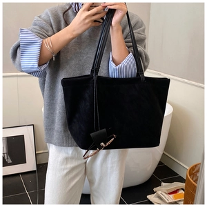 Detail of a large black suede tote bag with slim shoulder straps and sleek textured finish