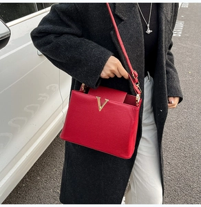 Détail du sac à main en cuir rouge avec boucle en V dorée et longue bandoulière