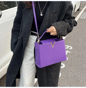 Détail d'un sac à main violet en cuir grainé avec logo V doré porté par un mannequin