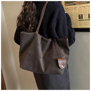 Detail of dark brown leather tote bag with long straps and a small buttoned pouch charm