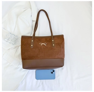 Detail of brown tote bag featuring a gold bow hardware and suede texture contrast