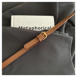 Gros plan d'une ceinture en cuir marron avec boucle dorée et surpiqûres détaillées