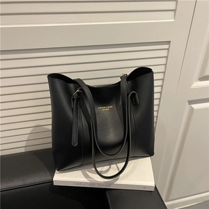 Minimalist black leather tote bag with gold lettering shown in a stylish home setting