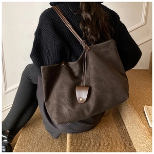 Detailed side view of dark brown matte tote bag with shoulder strap and gold rivet charm