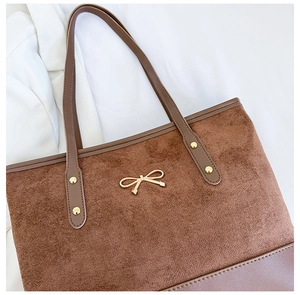 Detail of brown suede tote bag with gold bow ornament and leather trim and rivets
