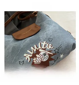Detail of washed blue denim shoulder bag with retro baseball print and leather flap texture
