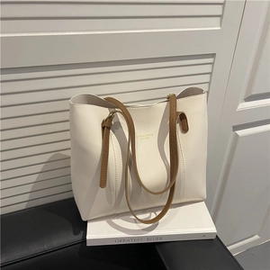 Minimalist cream leather tote bag with brown straps and gold lettering on white stand
