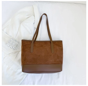Close-up of brown suede and leather tote bag styled with white blazer and glass decor