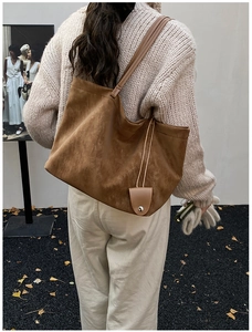 Detail of a large brown suede tote bag with slim shoulder straps and a leather tag