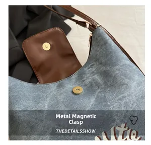 Close-up of magnetic snap closure on denim tote bag with leather trim and printing