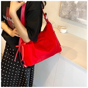 Detail of red nylon shoulder bag with wide strap and decorative bow ribbon accent