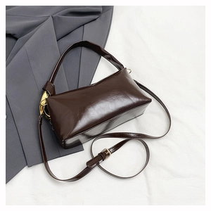 Detail of dark brown glossy leather pillow bag with gold metal hardware and shoulder strap
