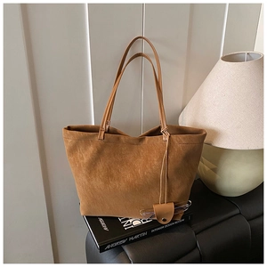 Detail of a brown suede tote bag with long straps and a leather glasses holder pendant