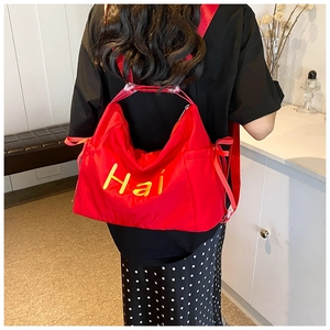Detail of red canvas tote bag with yellow Hai embroidery and wide shoulder strap