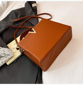 Détail du sac bandoulière marron caramel avec boucle dorée en V et texture en cuir grainé