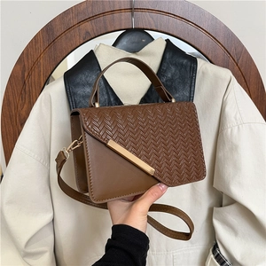 Brown leather crossbody bag with woven texture flap and golden buckle on autumn trench coat