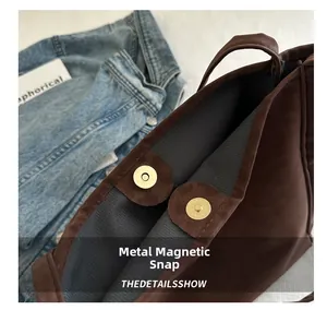 Detail of golden magnetic snap button and gray twill lining on brown suede tote bag