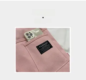 Detail of pink canvas bag side pocket with a phone and black logo label for casual use