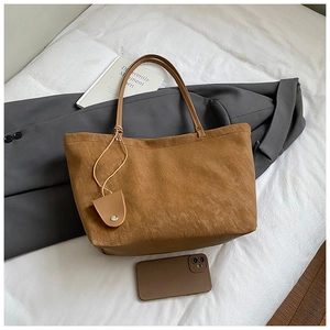 Detail of a brown suede tote bag with matching charm on white sheets with lifestyle props