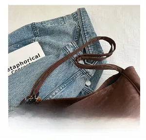 Detail of wide shoulder strap and woven charm on dark brown suede hobo bag