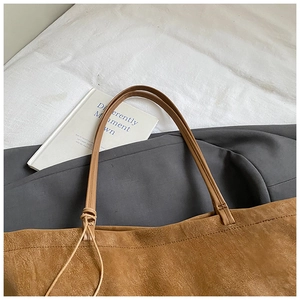 Detailed close-up of textured brown leather tote bag with slim shoulder straps