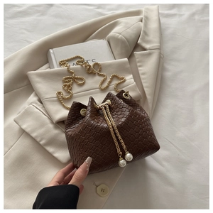 Dettaglio borsa a secchiello marrone scuro intrecciata con catena dorata e perle eleganti