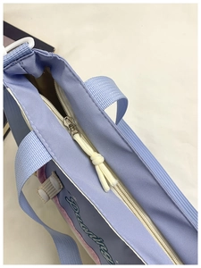 Detail of light blue canvas tote showing white zipper with cream knot pull and navy strap