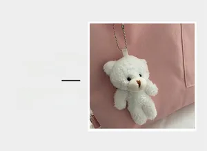 Detail magnification of a white plush bear pendant with a metal chain on a pink canvas bag