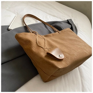 Detail of a brown suede tote bag with a small leather charm on white bedding