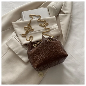 Dettaglio borsa a secchiello in pelle intrecciata marrone con catena dorata su beige