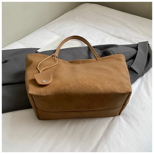 Detail view of the brown matte leather tote bag with thin handles and a semicircular charm